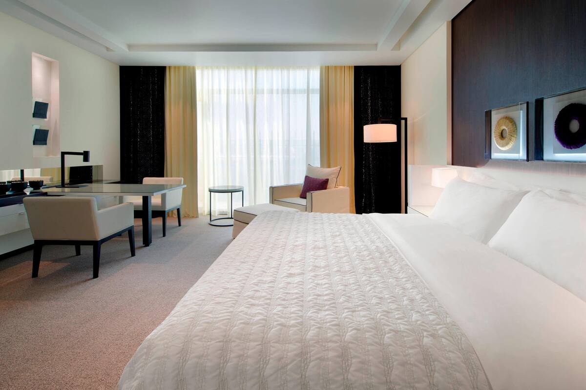 A hotel room with a large bed, a desk with a chair, a small table, and a sofa.