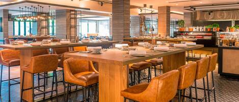 A modern bar area with wooden stools and a long counter, equipped with various bar tools and a display of bottles.