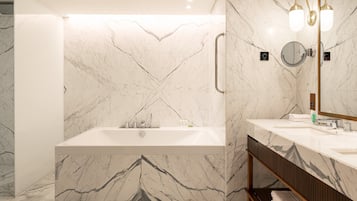 A modern bathroom with a marble wall, a freestanding bathtub, a vanity with a mirror, and a towel rack.