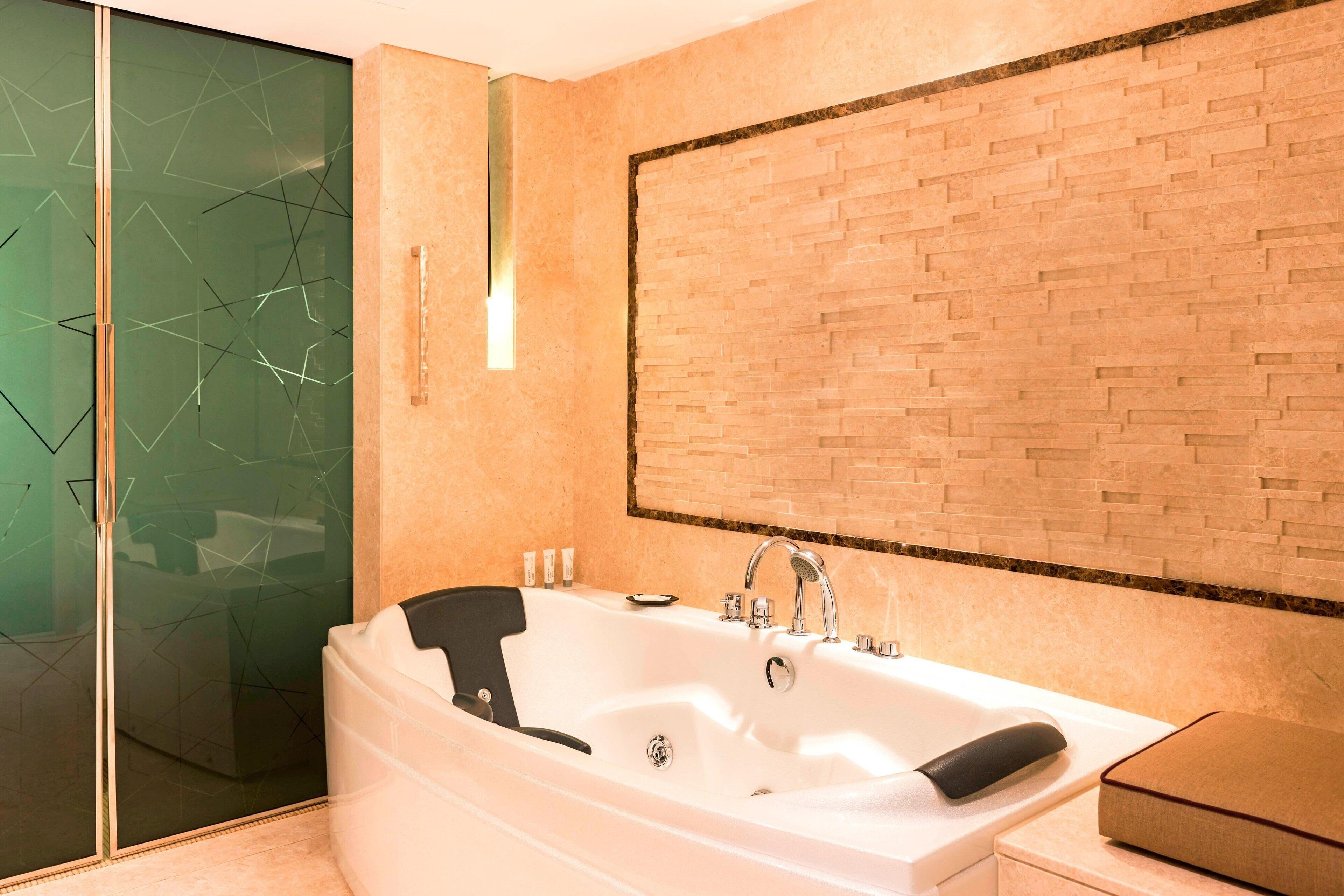 A modern bathroom with a large bathtub, a glass shower enclosure, and a brick-patterned wall.