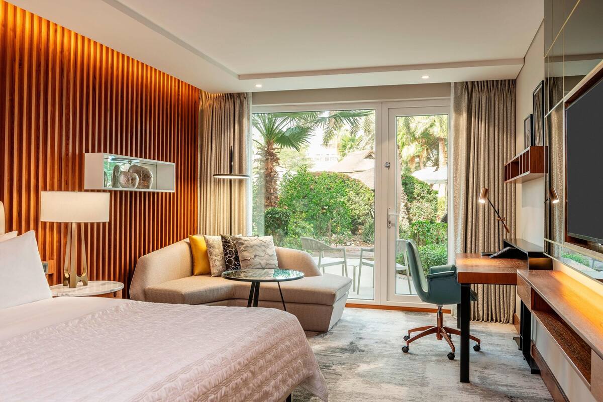 A hotel room with a bed, a sofa, a desk, and a view of the outdoors.