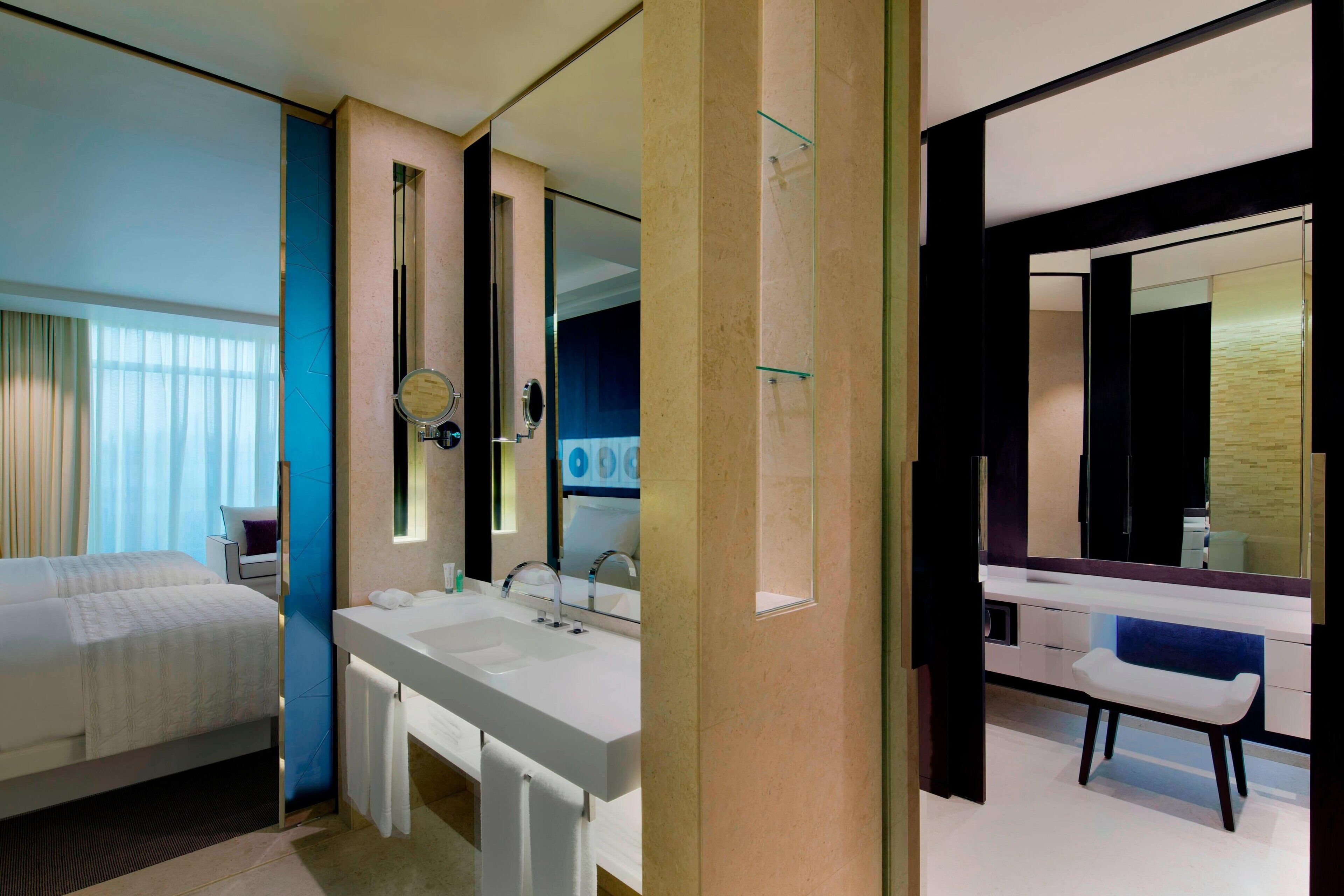 A modern hotel room with a large bed, a double sink, and a large mirror.