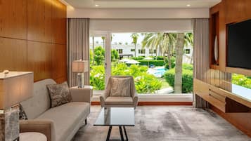 Uma sala de estar moderna com sofá, poltrona e mesa de centro, uma TV fixada na parede, e vista para uma piscina e área verde lá fora.