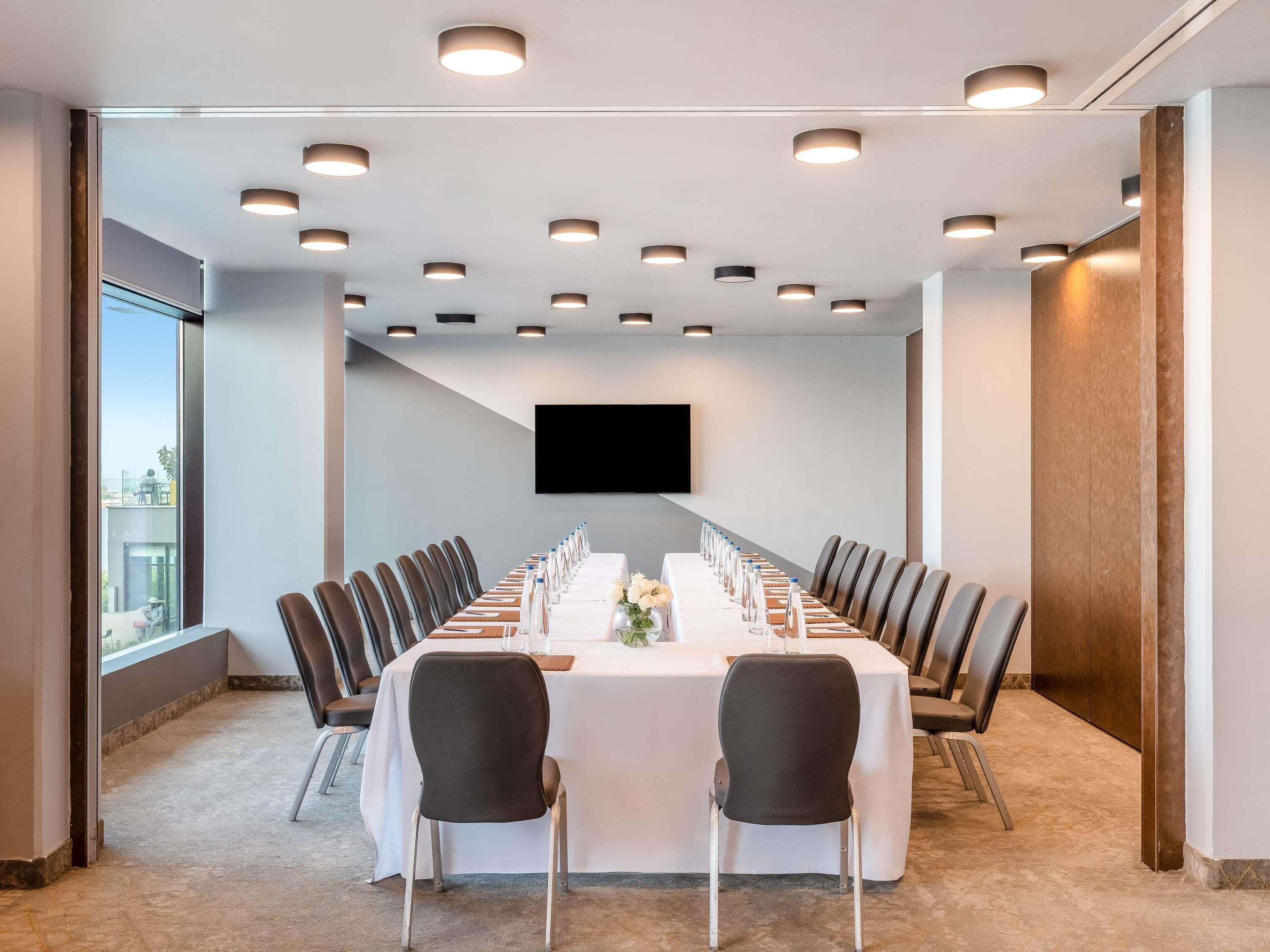 Una sala de conferencias con una mesa larga, sillas, un televisor de pantalla plana y luces empotradas en el techo.
