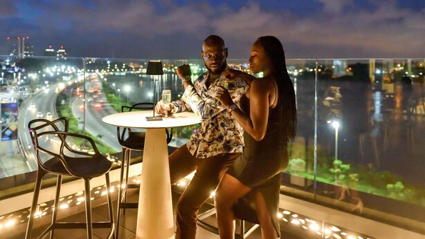 A couple dining at a table with a view of a cityscape and a river at night. - Pullman Abidjan (Abidjan)