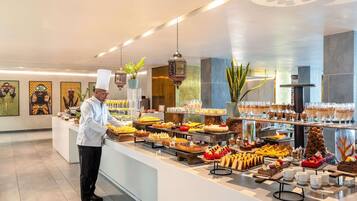 A buffet with various desserts and beverages, a chef preparing food, and decorative wall art.
