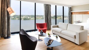 A modern living room with a white sofa, a red chair, a black armchair, a small table with a bottle and glasses, and a lamp. - Pullman Abidjan (Abidjan)