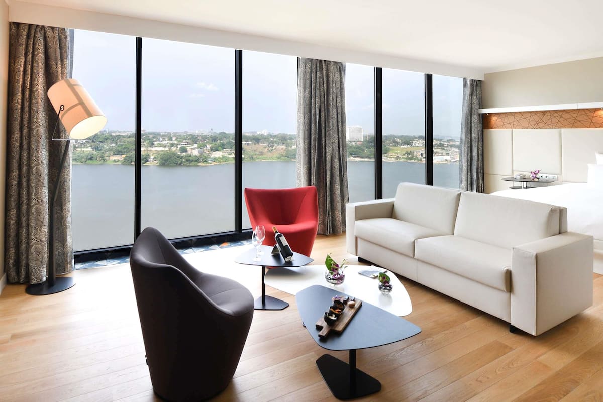 A modern living room with a white sofa, a red chair, a black armchair, a small table with a bottle and glasses, and a lamp.