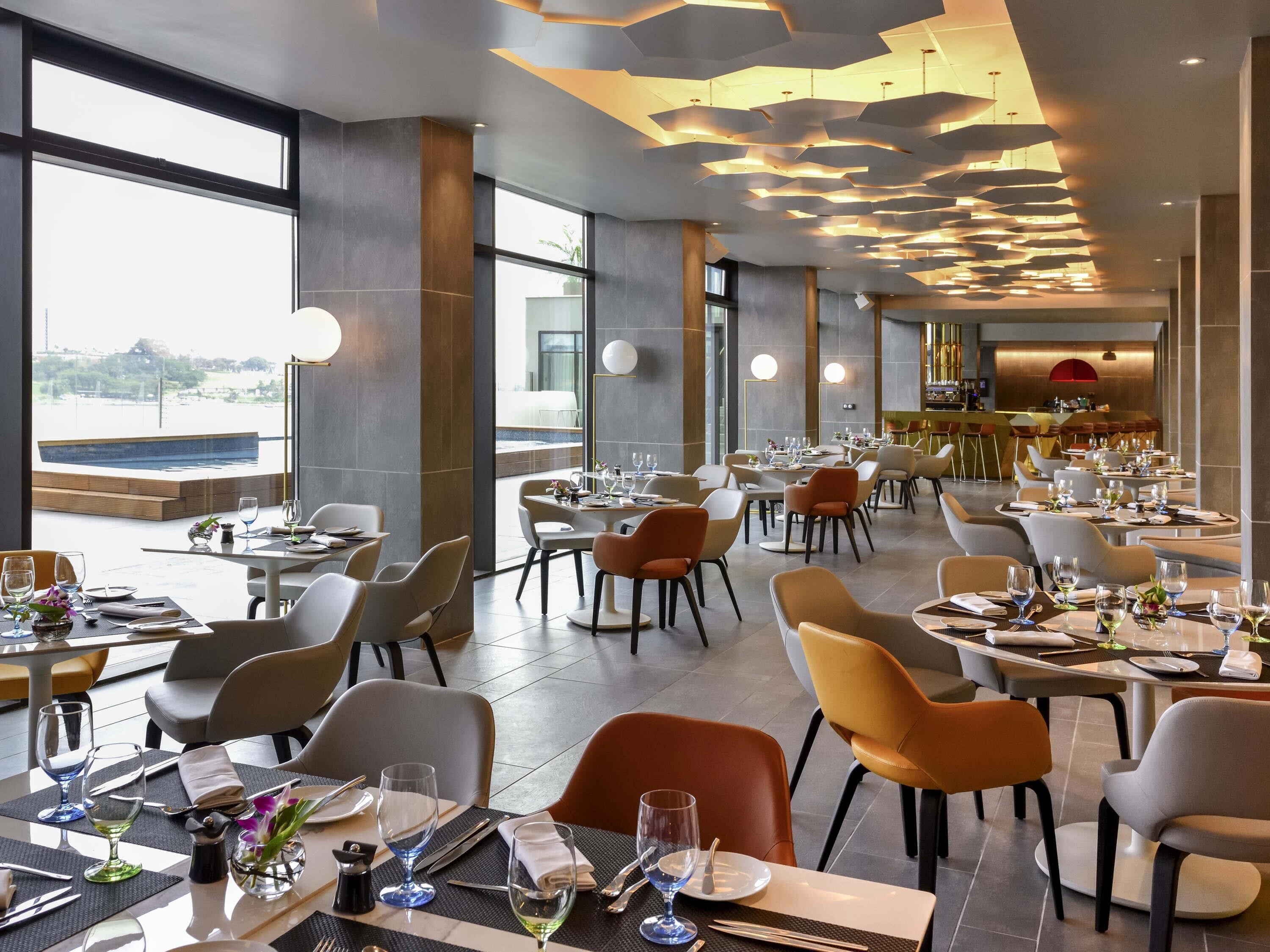 A modern restaurant with a view of the water, large windows, and a unique ceiling design.