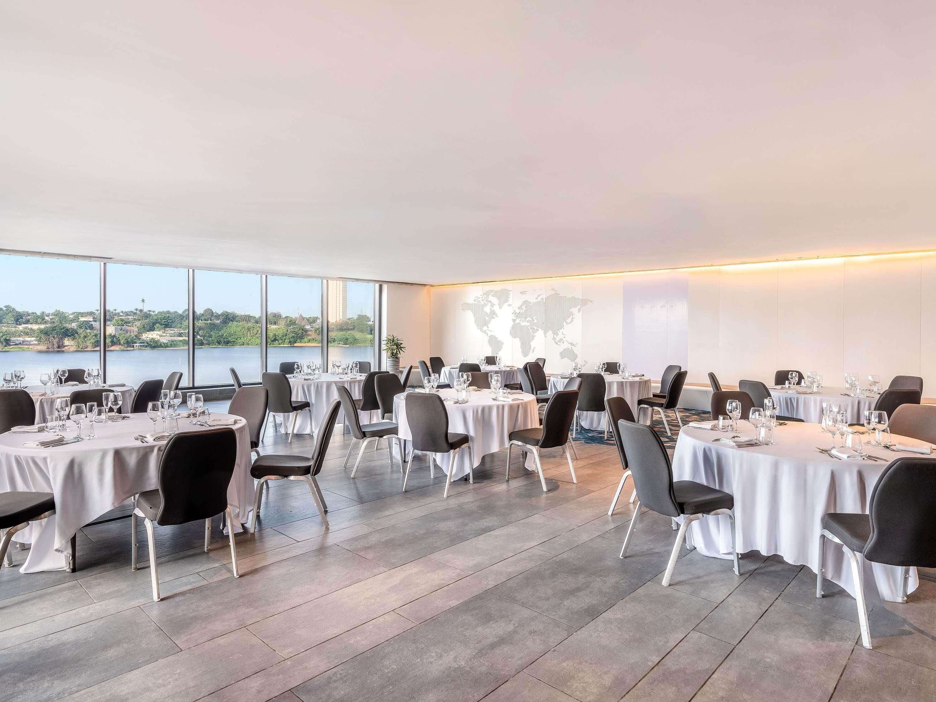 A dining area with tables set for a meal, chairs, and a large window with a view of a body of water and greenery.