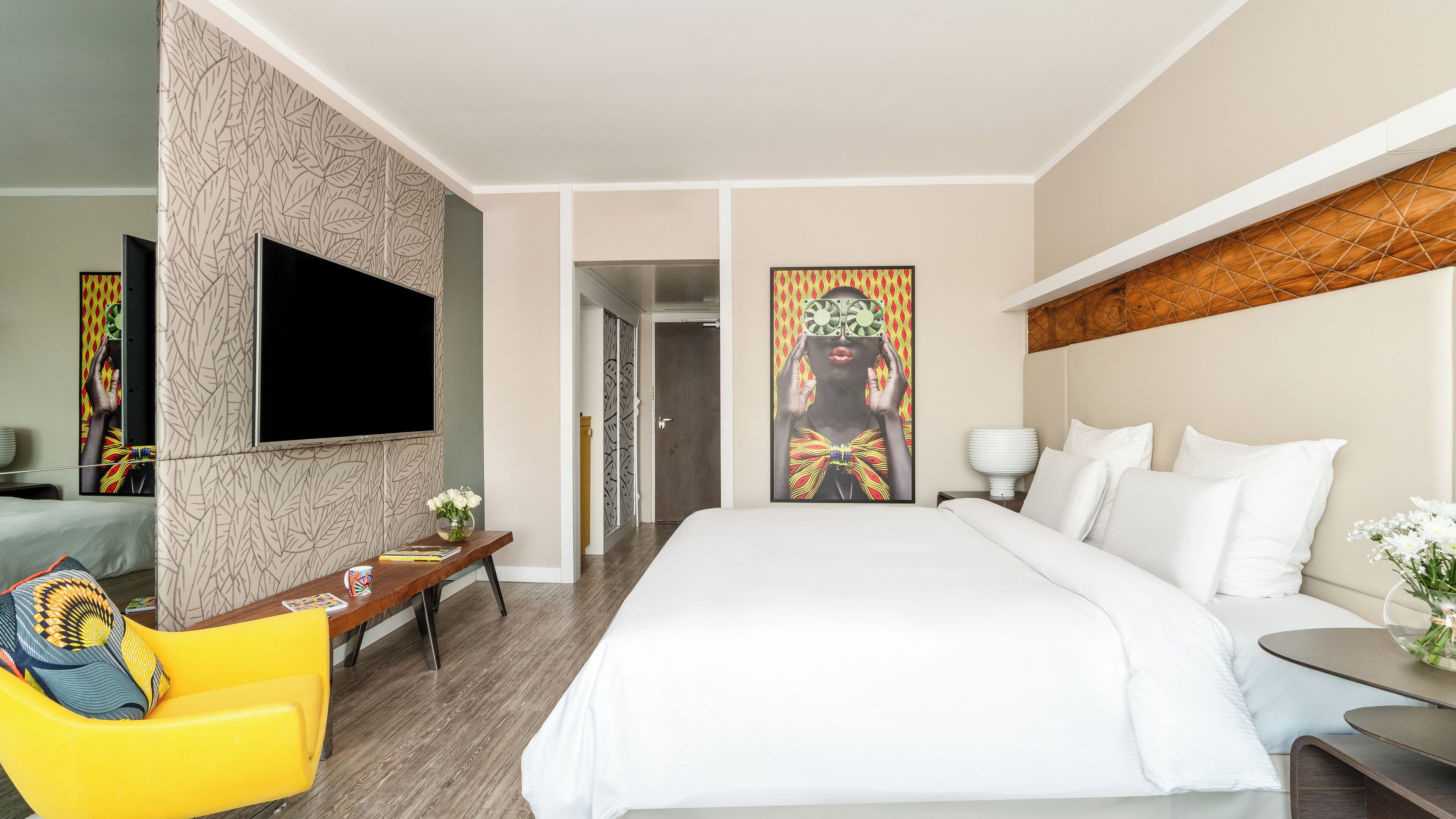 A hotel room with a bed, a desk, a chair, a TV, and artwork on the walls.
