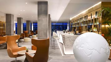 A modern hotel lobby with seating areas, a large globe sculpture, and a bar with a view of the city.