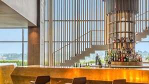 A modern bar area with a bar counter, three stools, and a variety of bottles. - Pullman Abidjan (Abidjan)