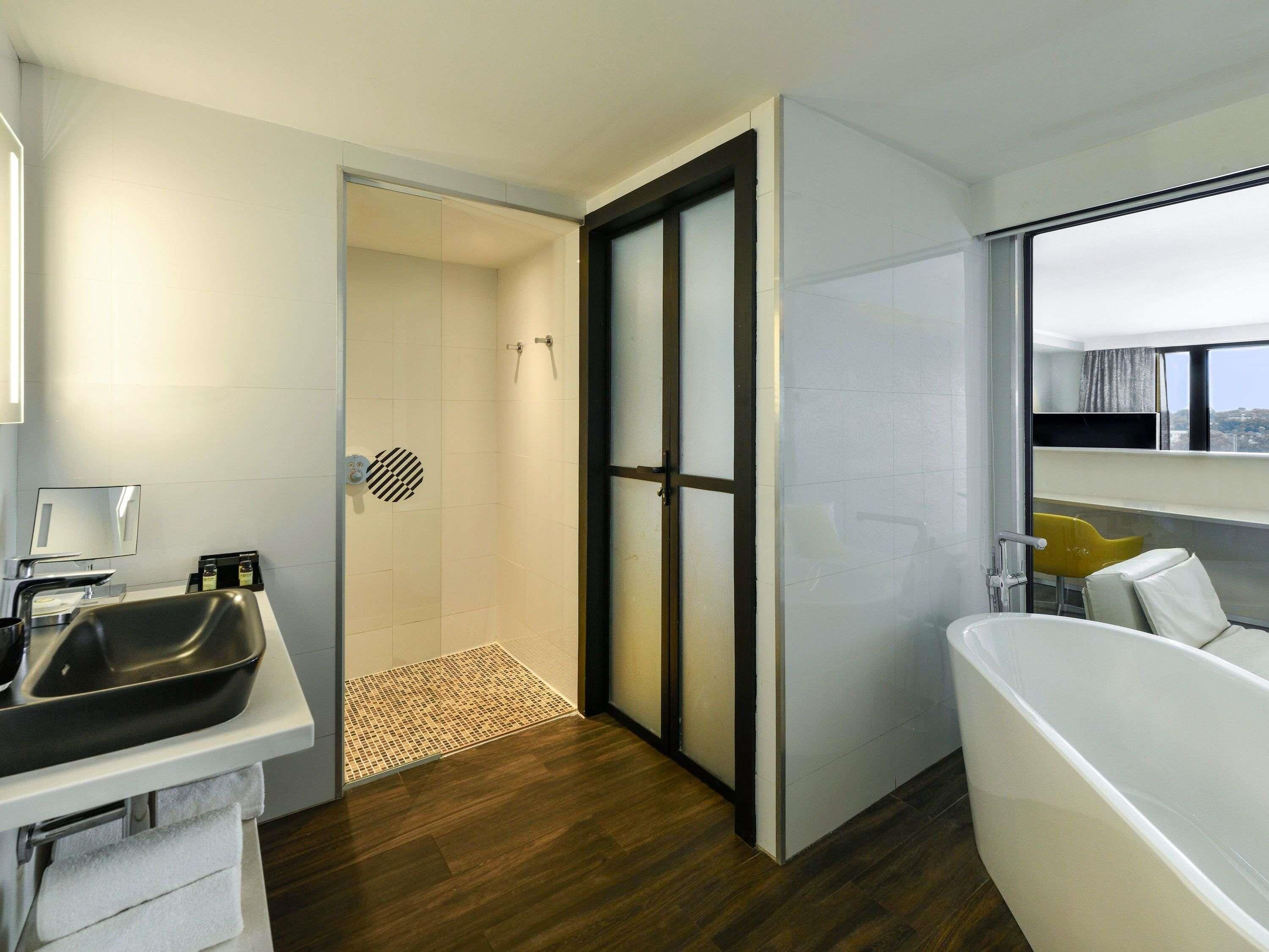 Un baño moderno con bañera, ducha y lavabo. Una ventana ofrece vistas a la ciudad.