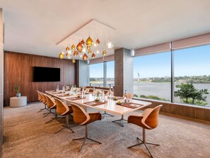 A conference room with a long table, modern chairs, a flat-screen TV, and large windows with a view of a body of water. - Pullman Abidjan (Abidjan)