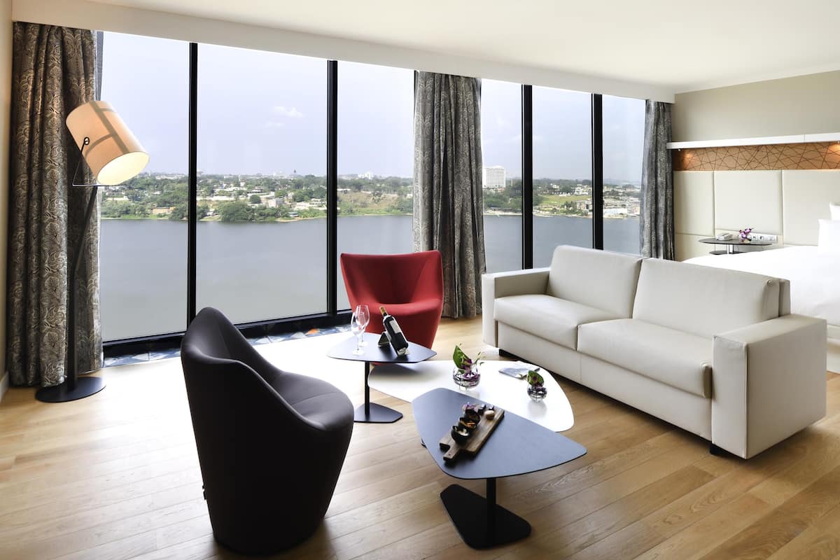 A modern living room with a large window, a red chair, a white sofa, and a small table with a bottle and glass.