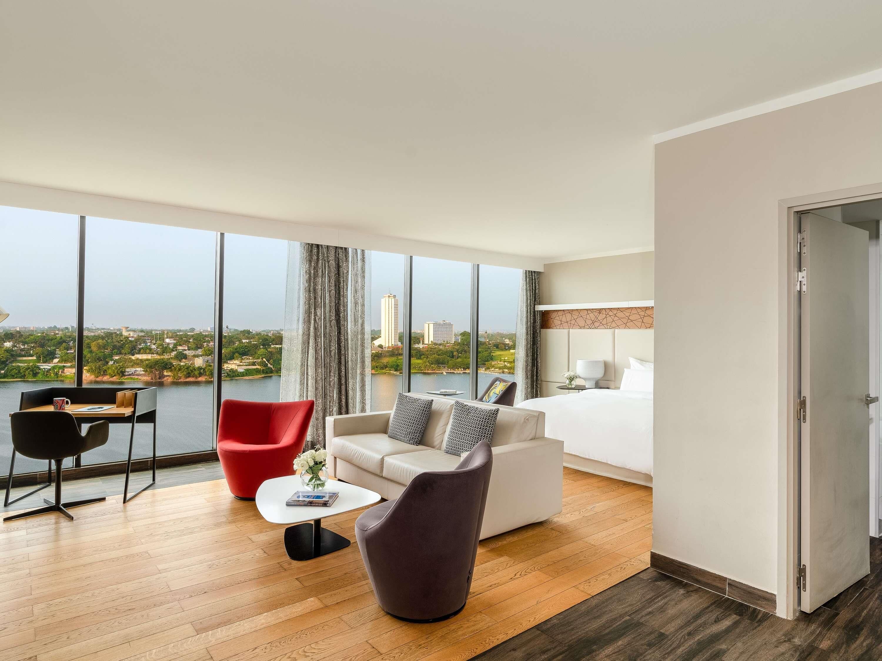 A hotel room with a large window, a bed, a desk, and two chairs.