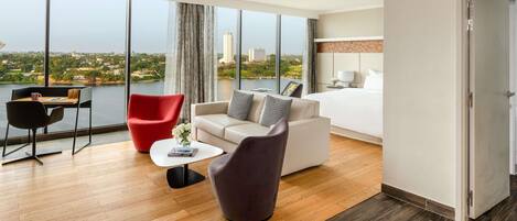 A hotel room with a large window, a bed, a desk, and two chairs.