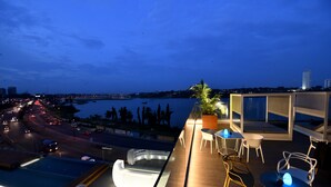 A rooftop terrace with a pool, seating area, and a view of the cityscape and water at dusk. - Pullman Abidjan (Abidjan)