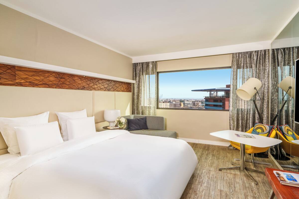 A hotel room with a large bed, a small sofa, a table with a lamp, and a TV.