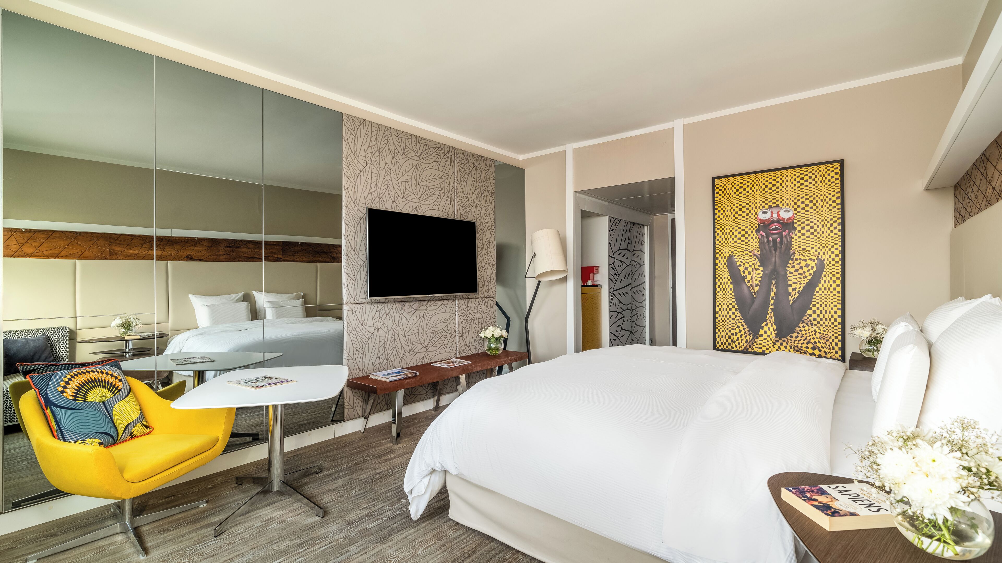 A hotel room with a large bed, a desk, a chair, a TV, and a mirror.