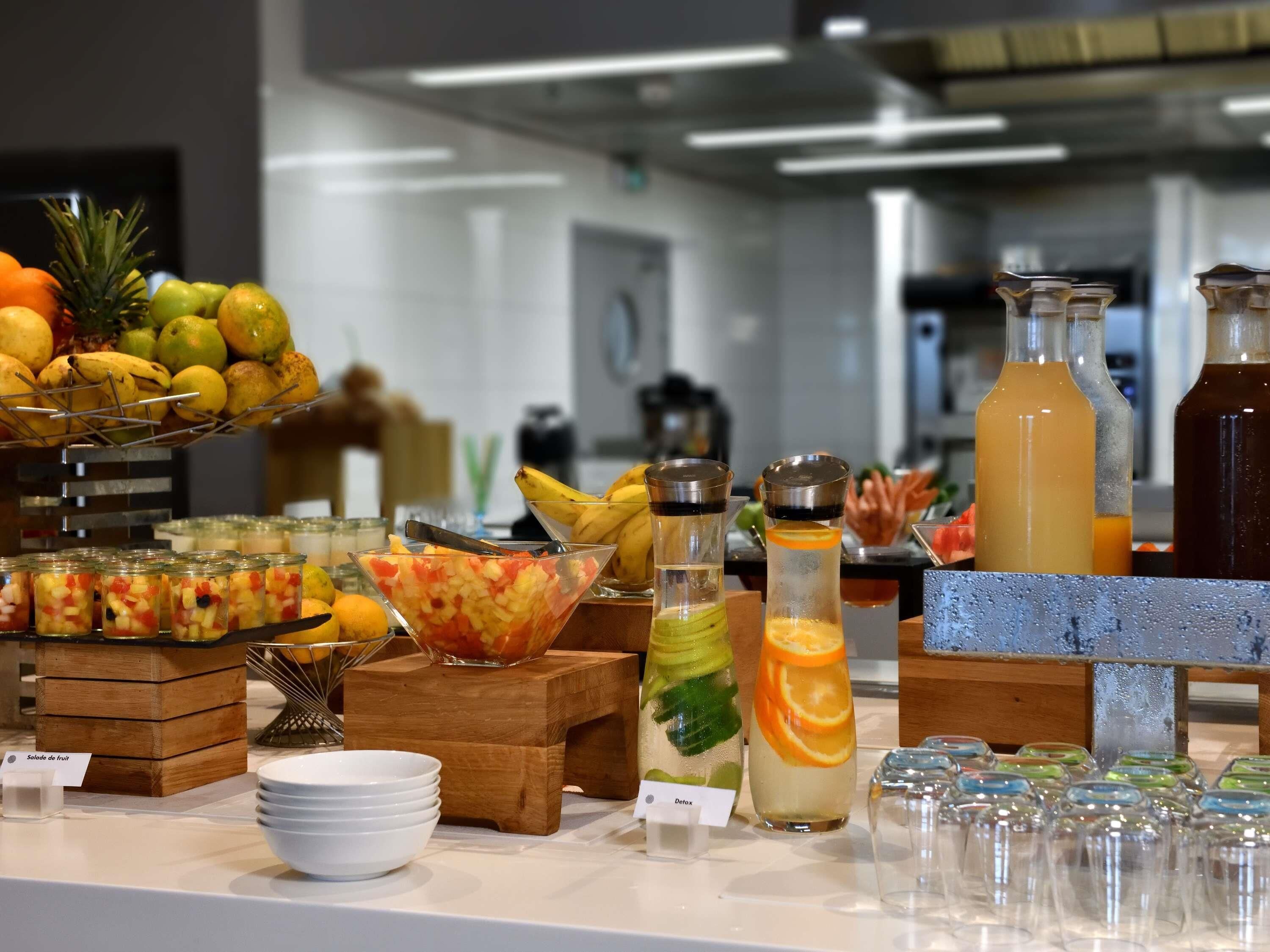 Un buffet con diversi tipi di frutta, una ciotola di insalata di frutta mista e diversi erogatori di bevande.