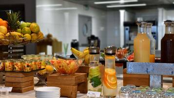 Un buffet con diversi tipi di frutta, una ciotola di insalata di frutta mista e diversi erogatori di bevande.