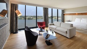 A modern hotel room with a large window, a white sofa, a red chair, a small table, and a bed. - Pullman Abidjan (Abidjan)