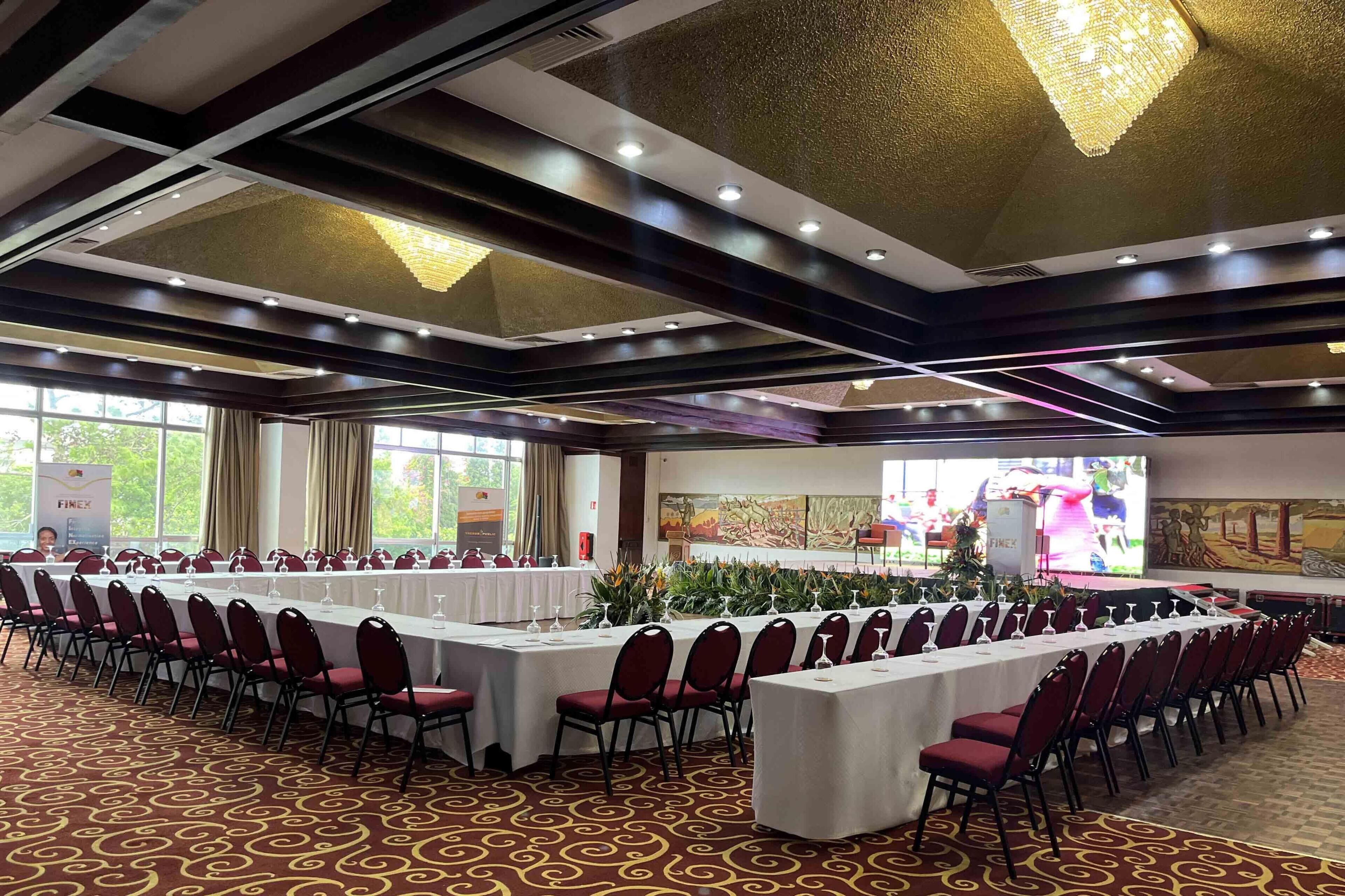 Une salle de banquet avec de longues tables, des chaises rouges et un tapis à motifs.