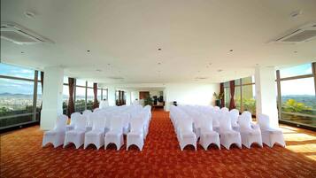 Un salón de conferencias con filas de sillas blancas, ventanas amplias y una alfombra roja.
