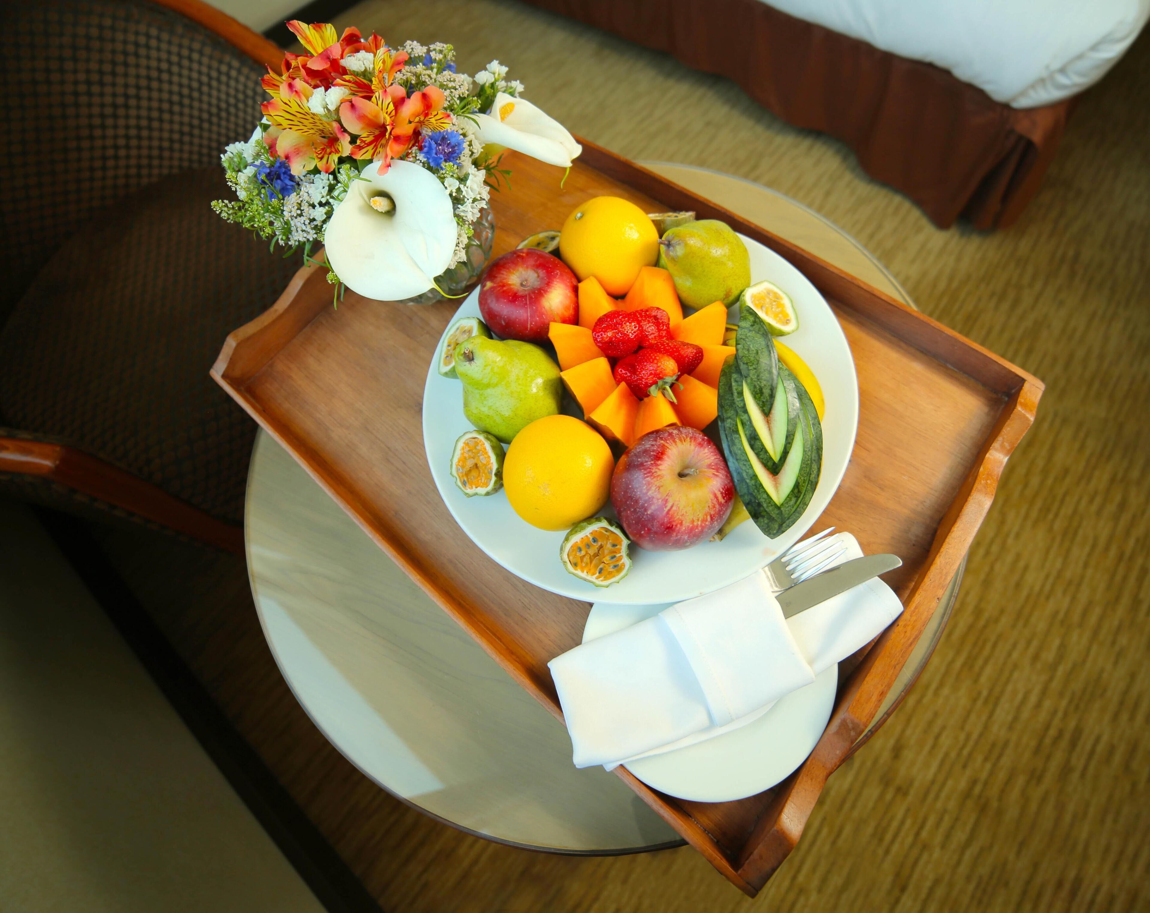 A tray with fruits and a flower arrangement on a round table.
