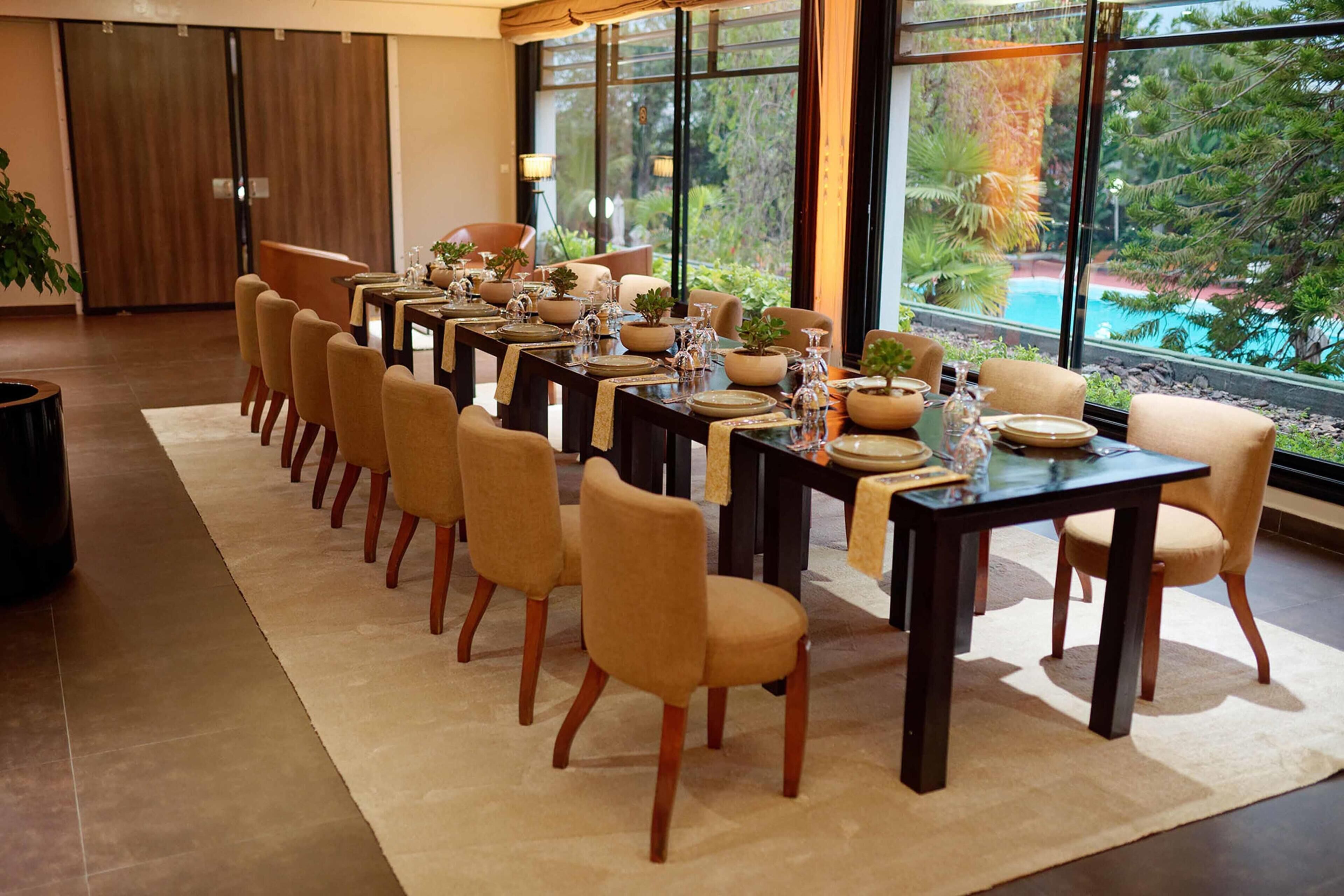 A dining area with multiple tables and chairs, large windows with a view of greenery, and a modern interior design.