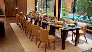 A dining area with multiple tables and chairs, large windows with a view of greenery, and a modern interior design.