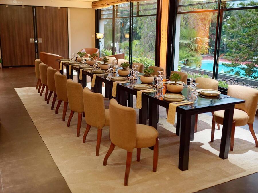 A dining area with multiple tables and chairs, large windows with a view of greenery, and a modern interior design.