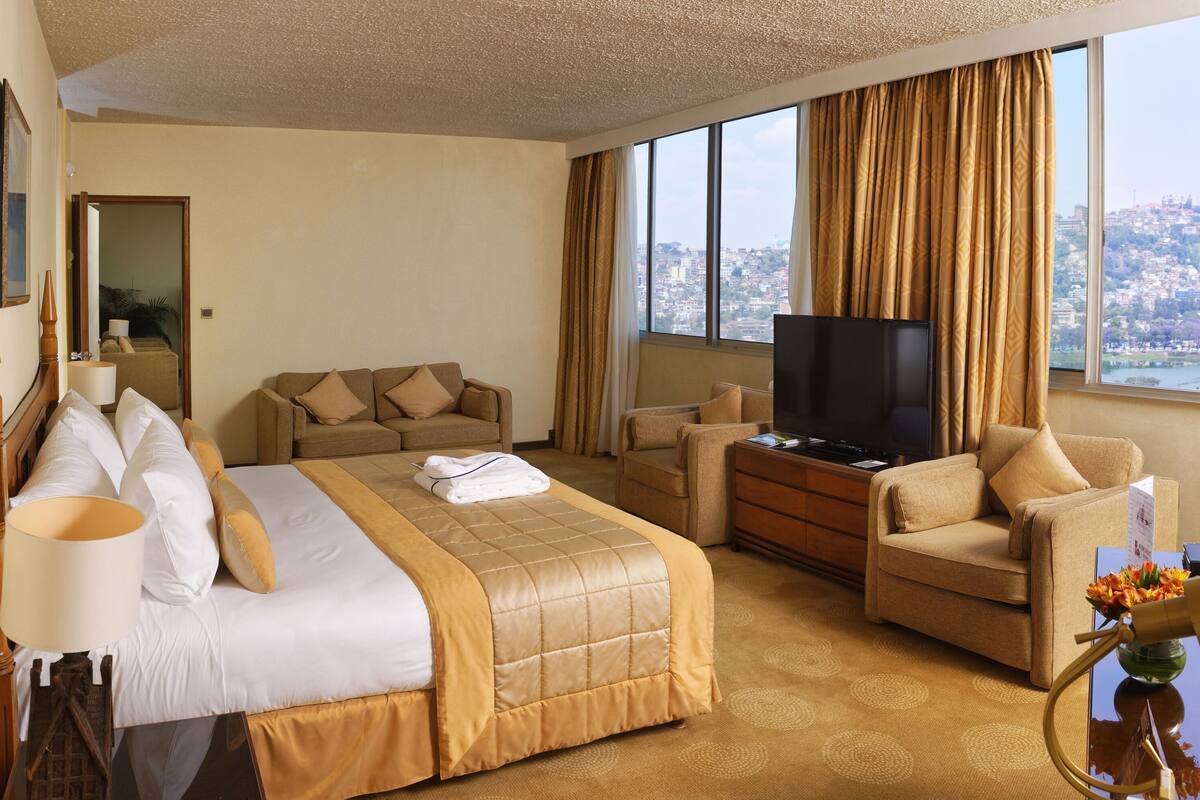 A hotel room with a bed, a sofa, a TV, and a view of a cityscape.