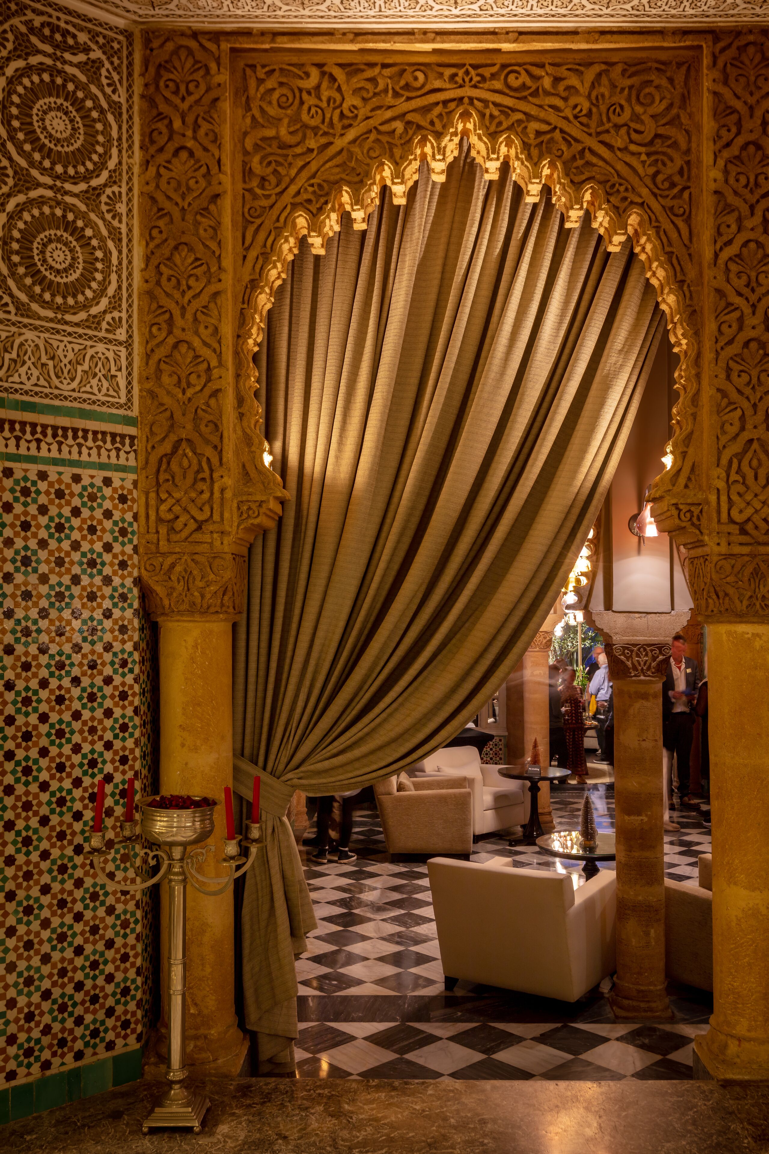Un interior ornamentado con suelo a cuadros, un cortinero drapeado y un candelabro.