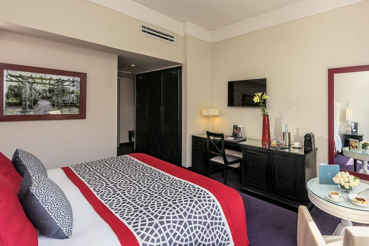 A hotel room with a bed, a desk, a chair, a round table, a TV, and a mirror.