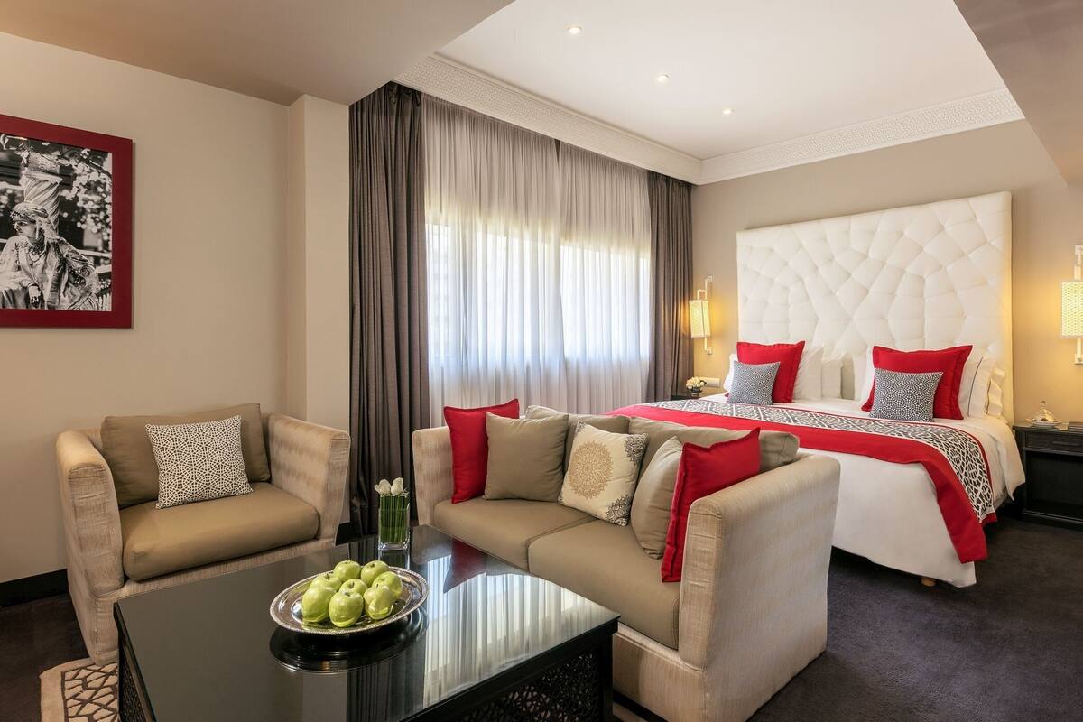 A hotel room with a large bed, two sofas, a coffee table with apples, and a framed picture on the wall.