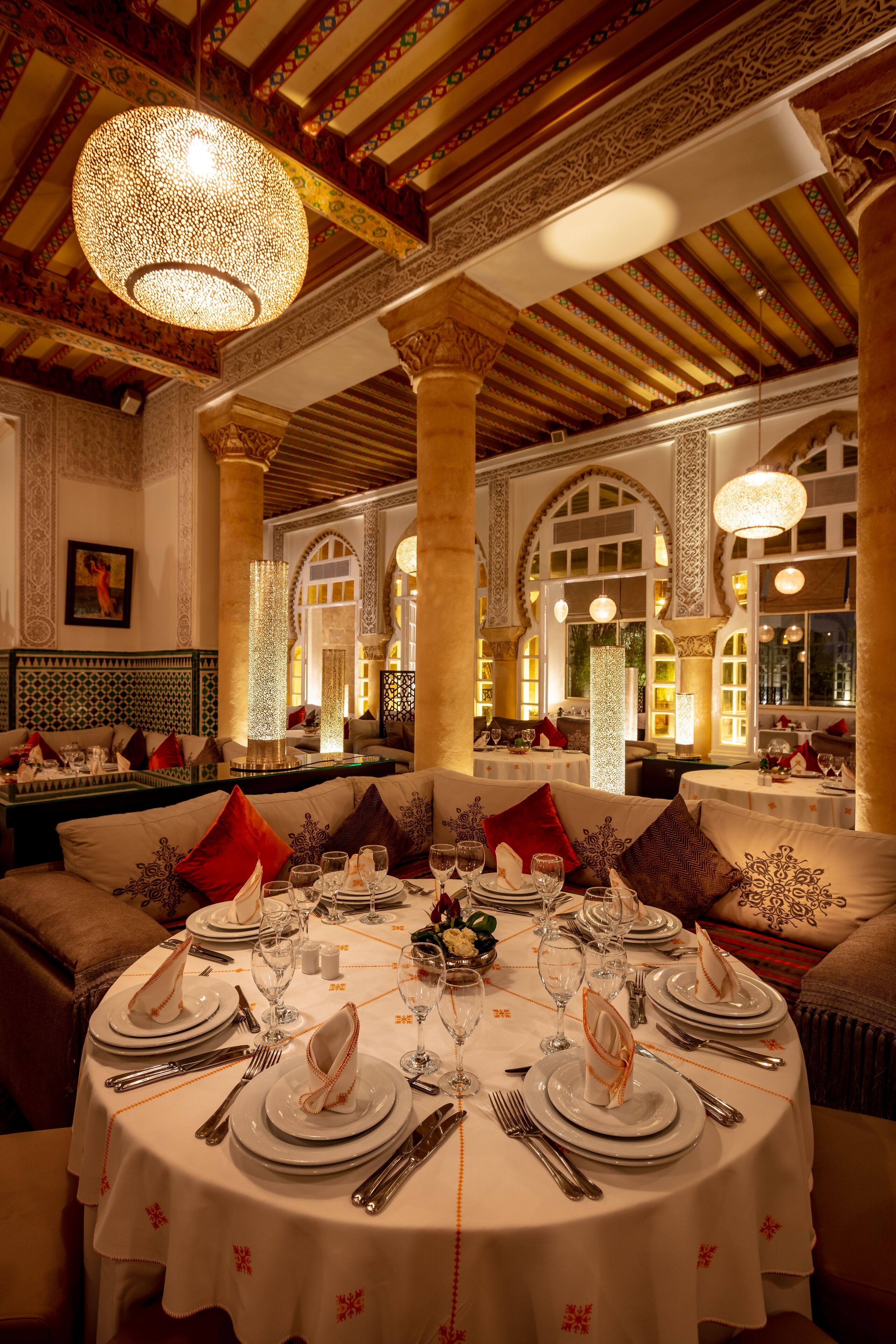 A luxurious dining area with ornate ceiling and columns, round tables set for a meal, and a warm, inviting atmosphere.