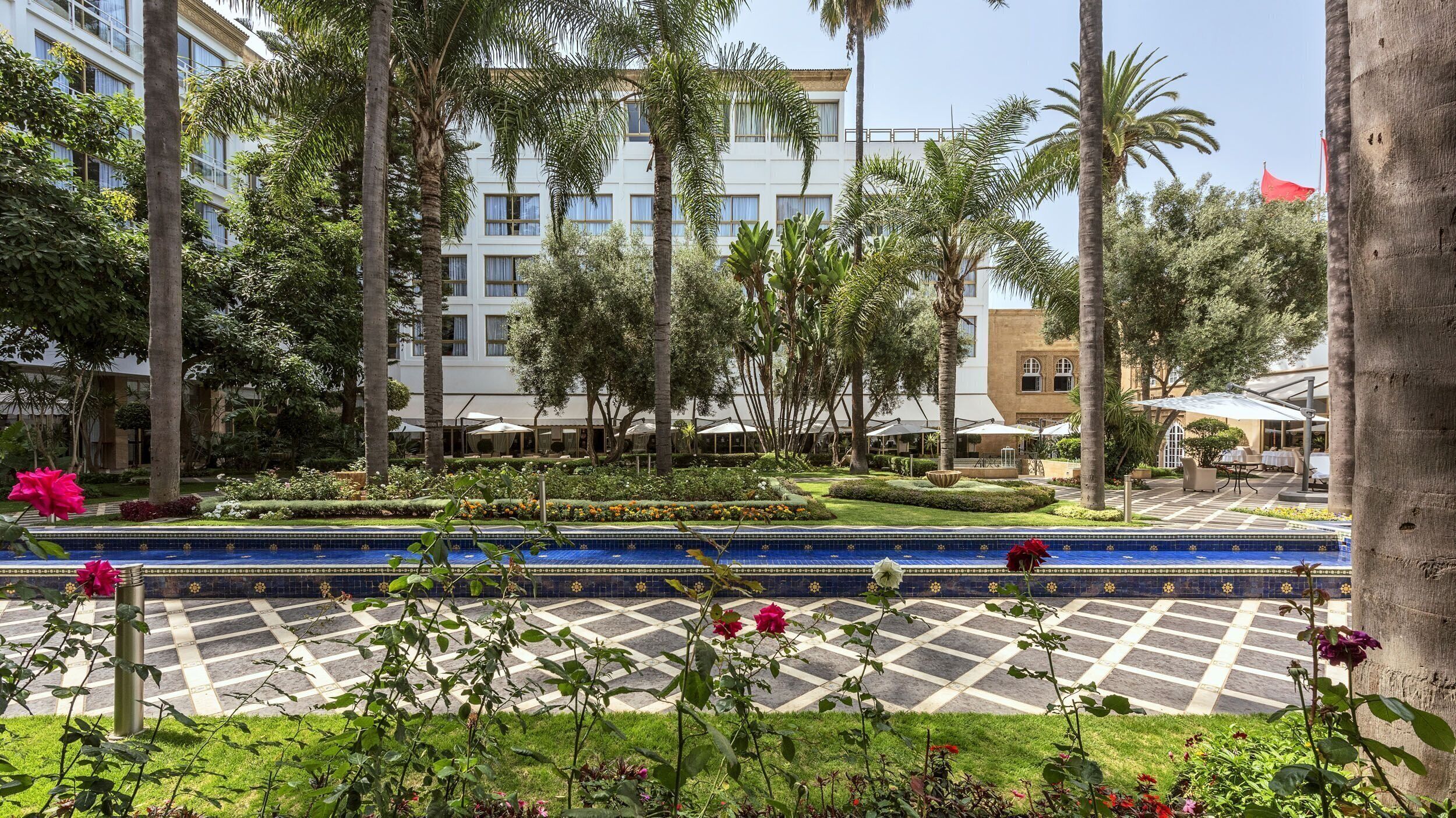 Un patio de hotel con piscina, palmeras y una bandera roja.