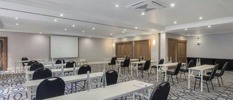 Un salón de conferencias con mesas, sillas, una pantalla de proyector y suelo alfombrado.