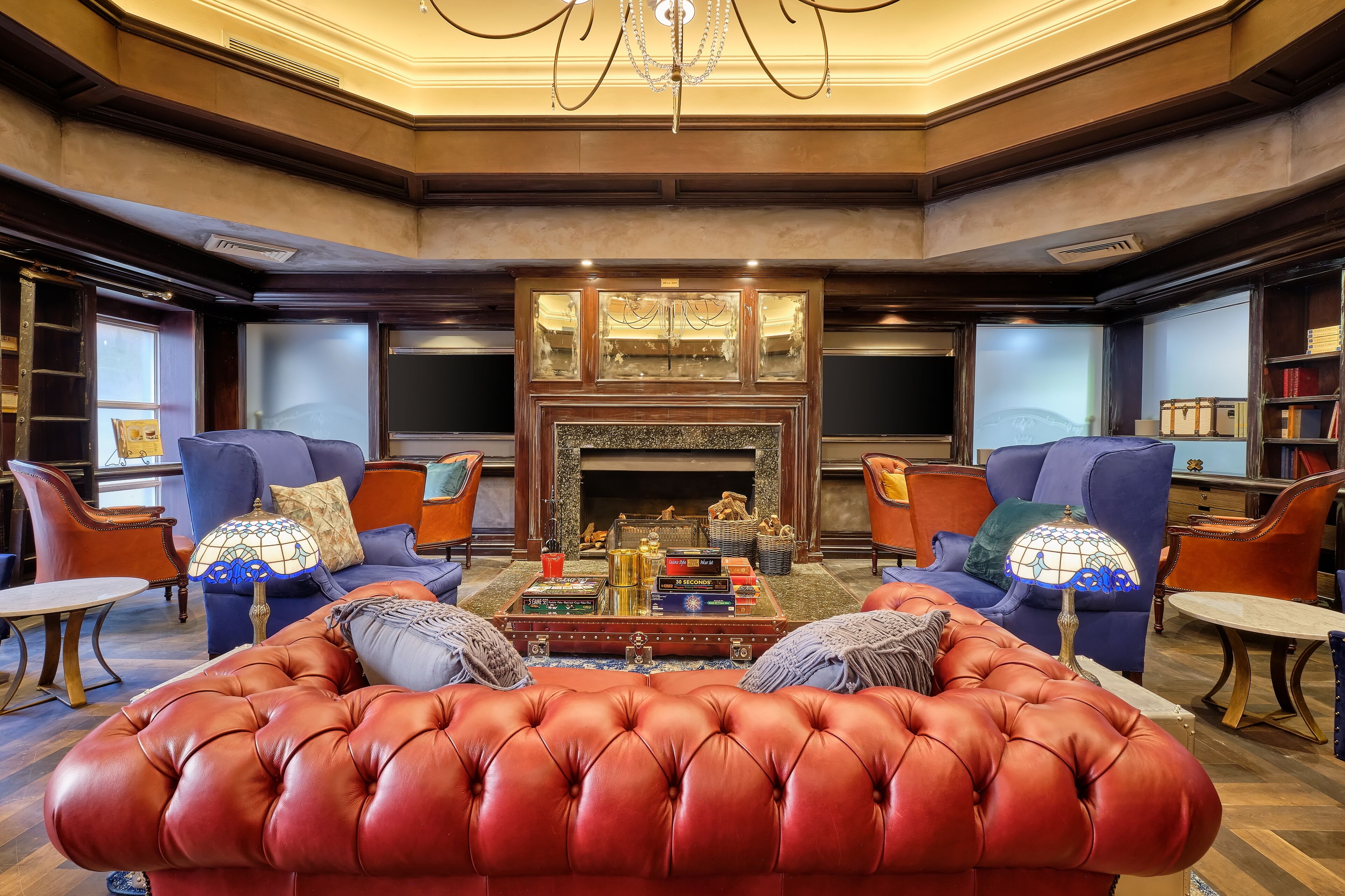 A luxurious living room with a red leather sofa, two armchairs, a coffee table with decorative items, and a fireplace.