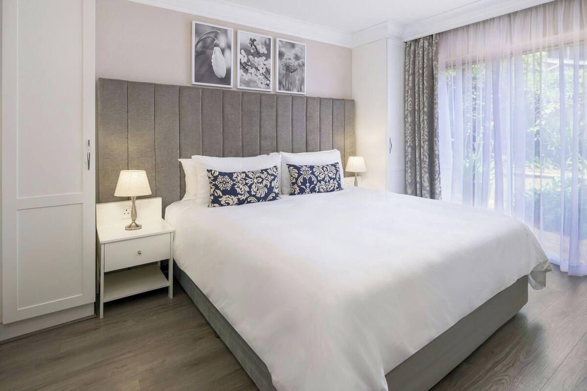 A neatly made bed with white and blue patterned pillows, a grey upholstered headboard, and a bedside table with a lamp.