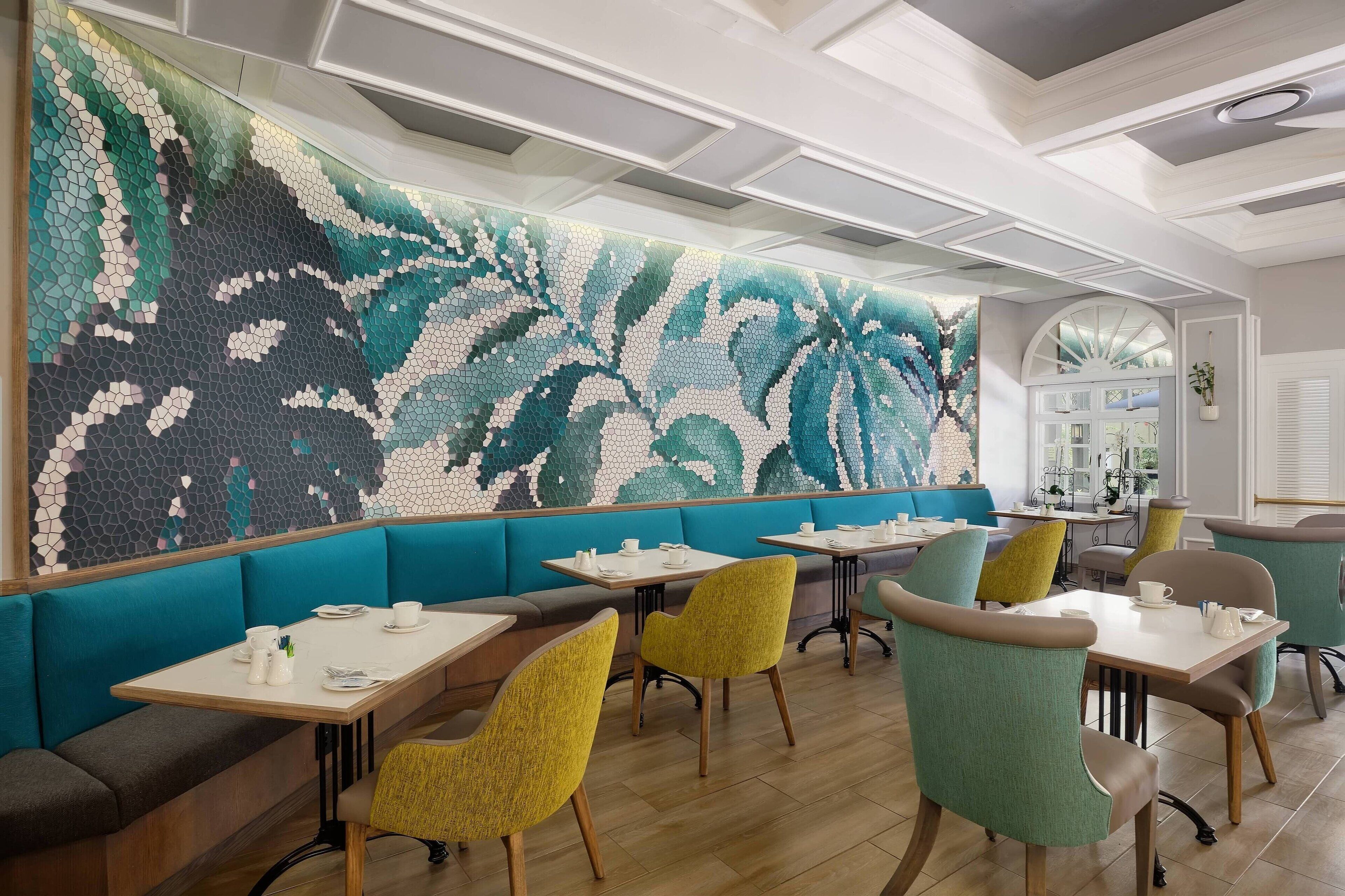 A modern restaurant with teal and gray seating, wooden tables, and a large mosaic wall.