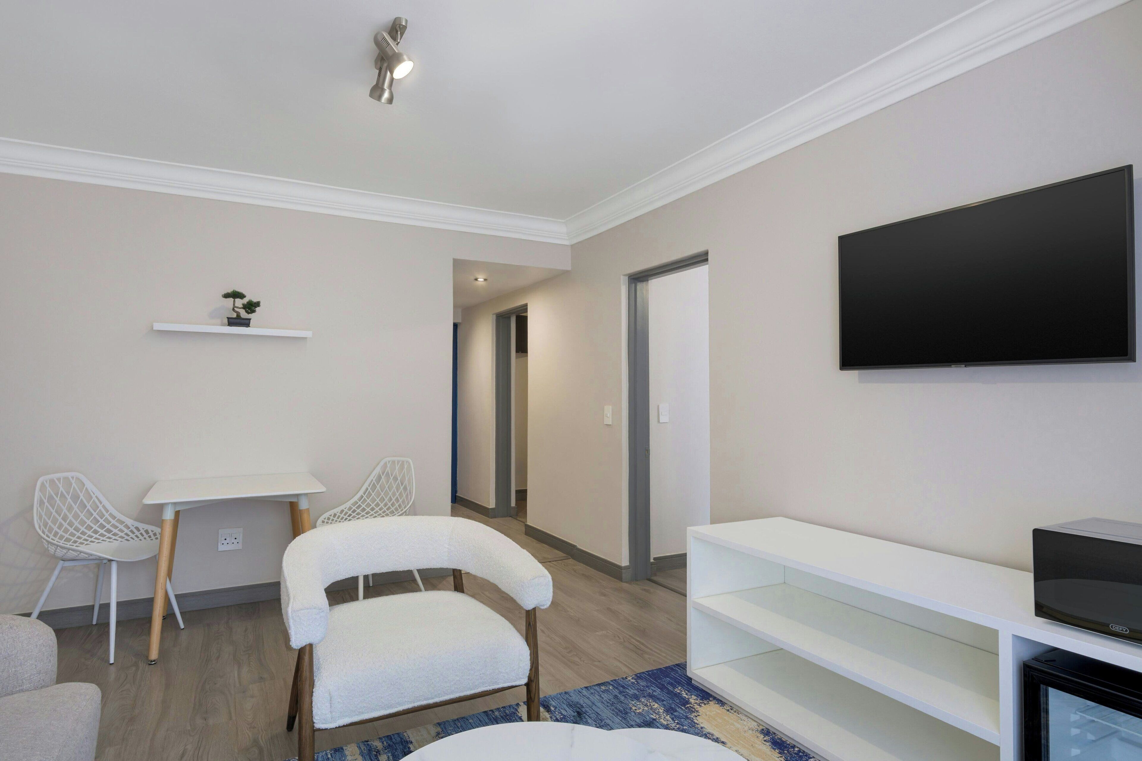 A modern living room with a flat-screen TV, white furniture, and a blue rug.