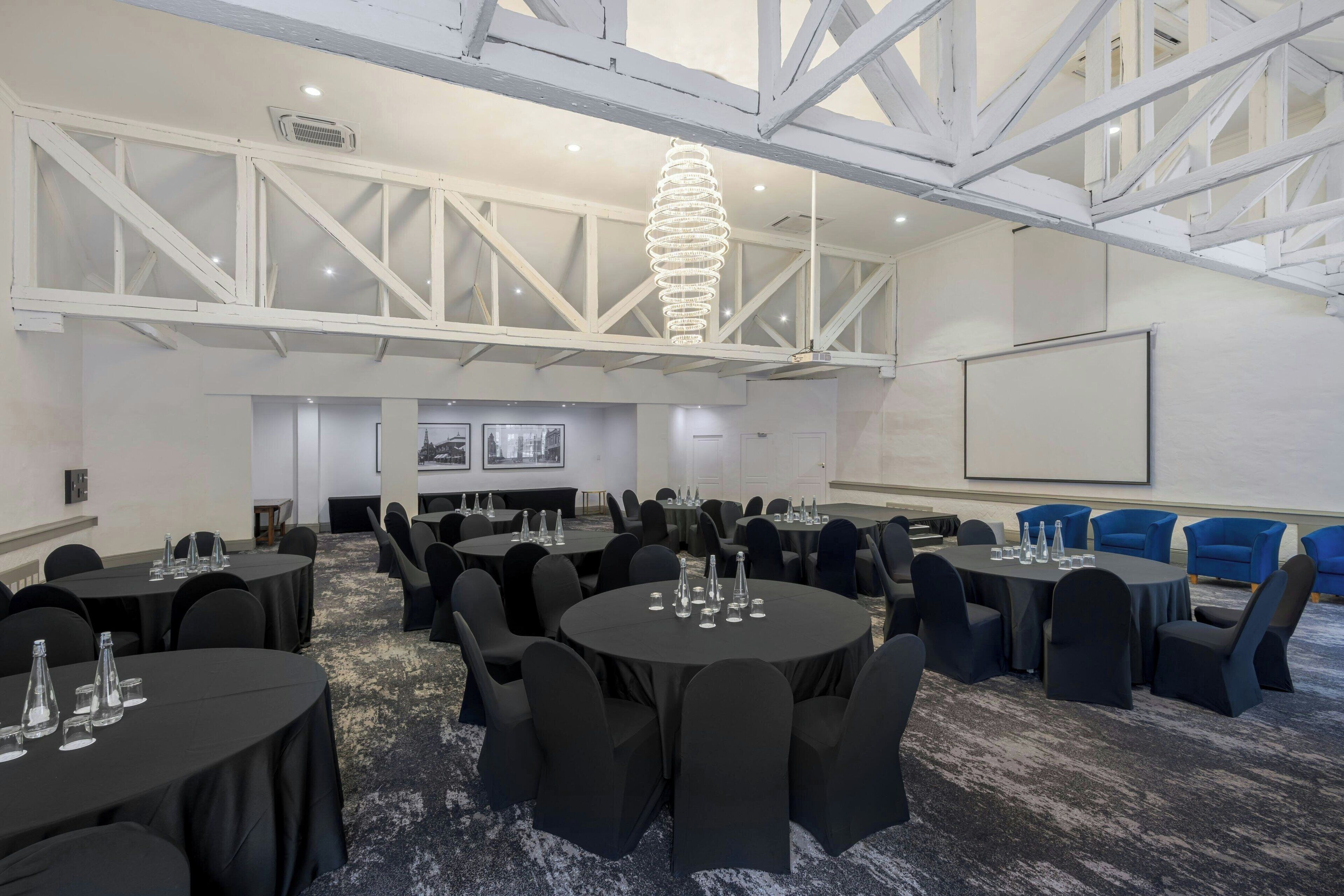 Une salle de conférence avec des tables rondes, des chaises noires et une structure de plafond blanche.
