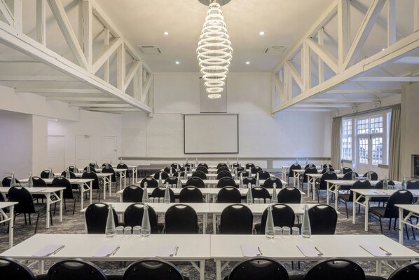 Un salón de conferencias con mesas blancas, sillas negras, una pantalla grande y una lámpara de araña.