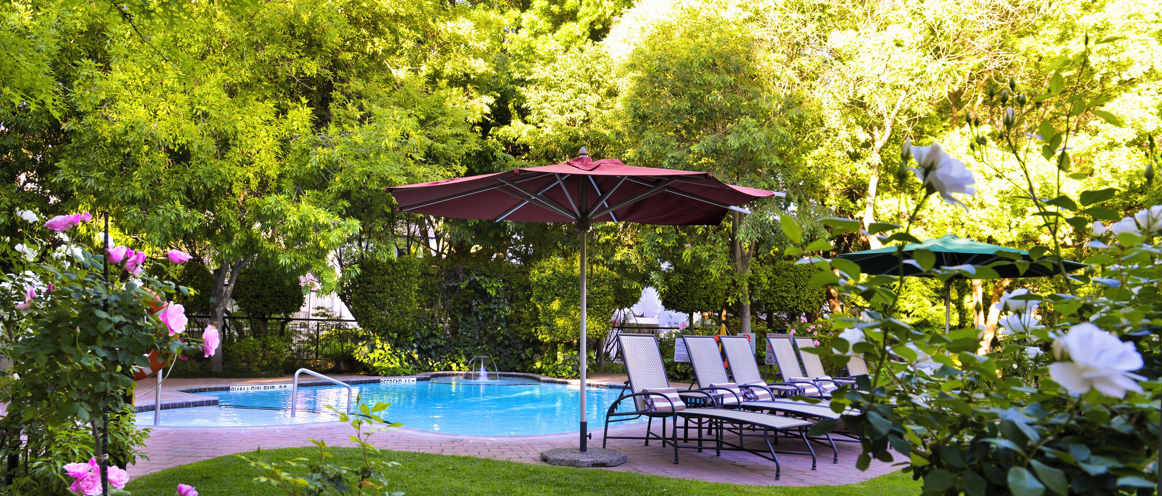 A swimming pool with lounge chairs and umbrellas, surrounded by lush greenery.