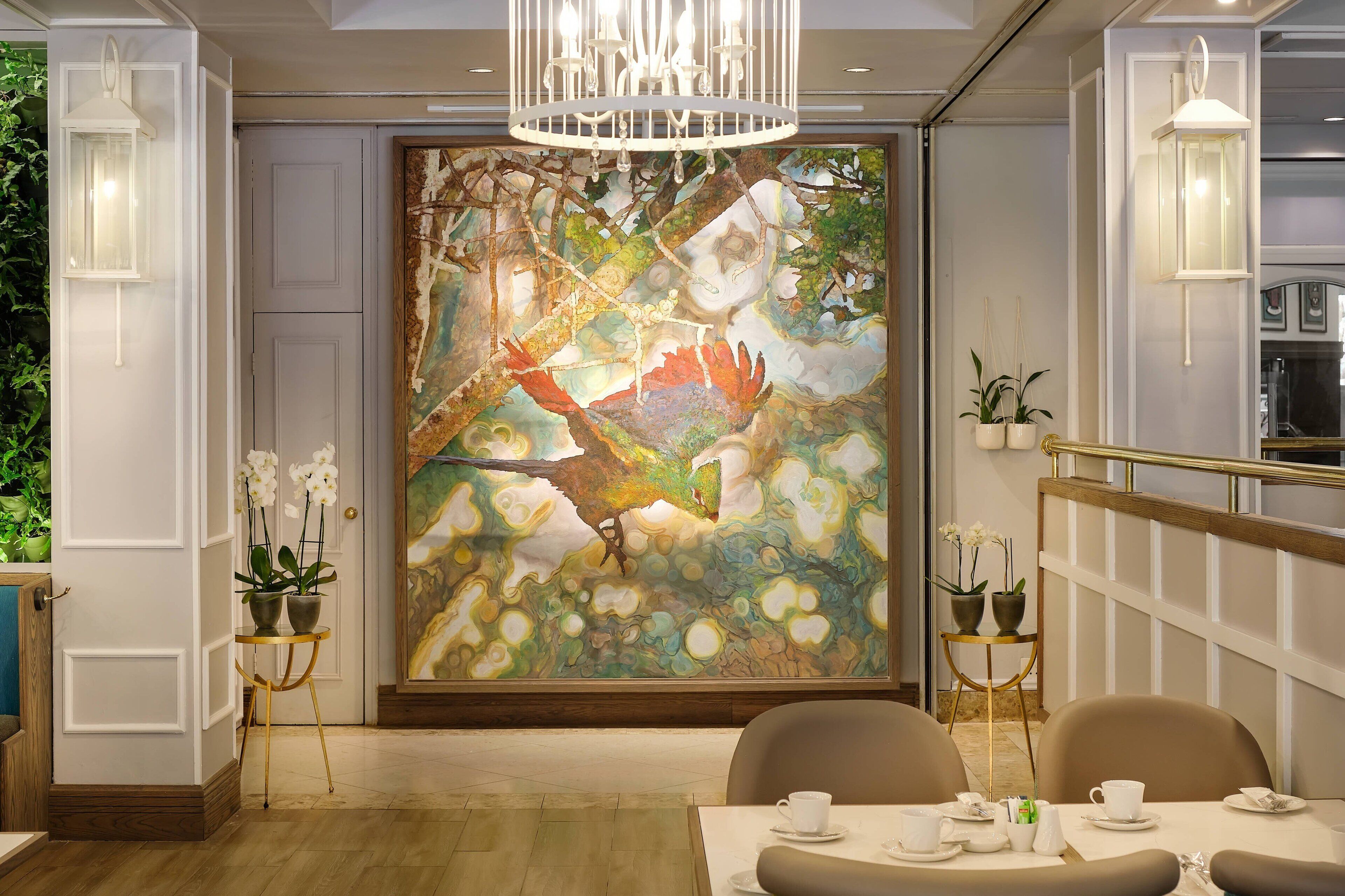 A dining area with a large abstract painting, two potted orchids, and a chandelier.