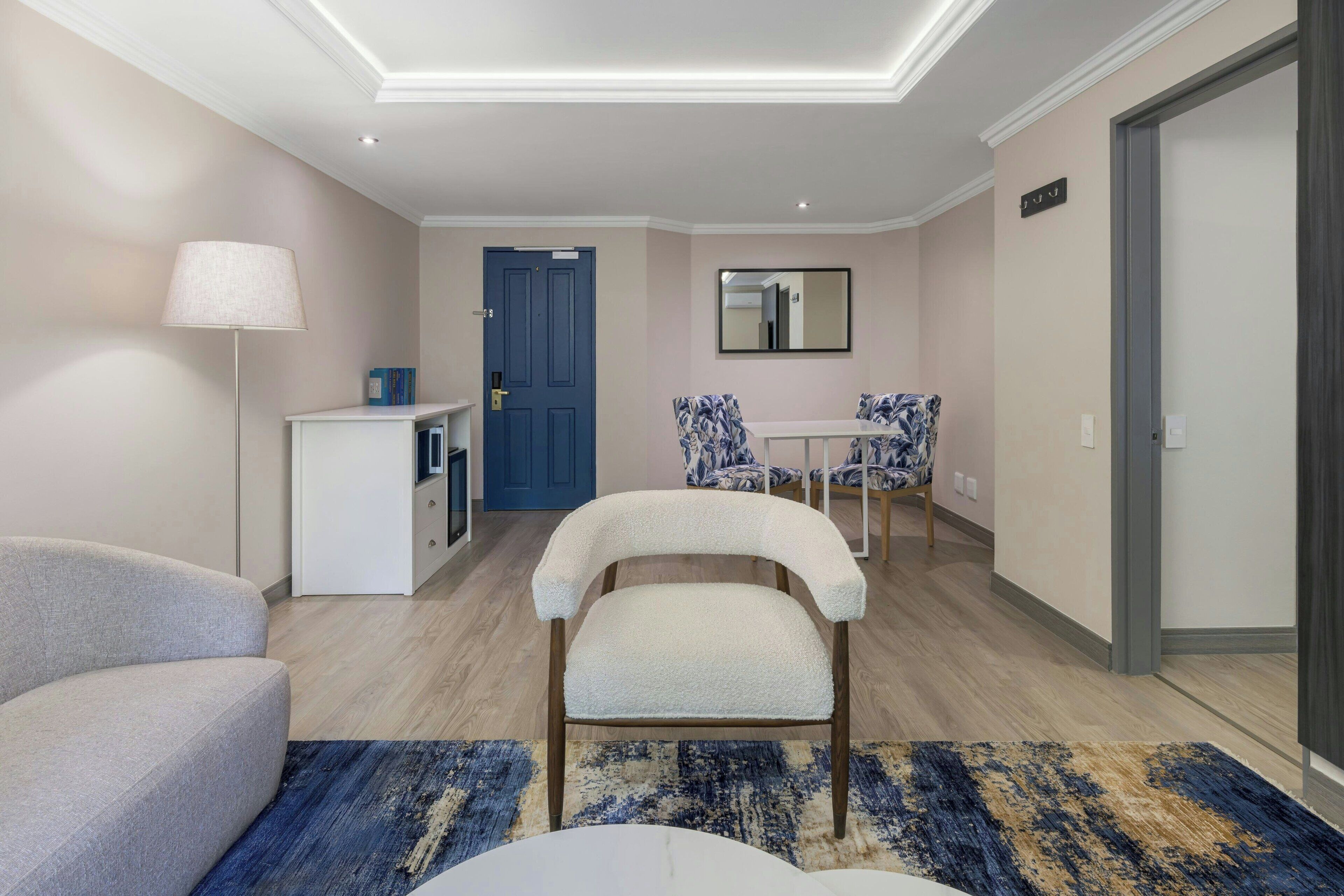 A modern hotel room with a sofa, a small table, a chair, a lamp, and a mirror.